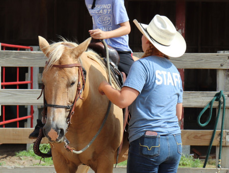 Rock Springs Ranch camp counselor assisting a camper who is preparing for a trail ride.