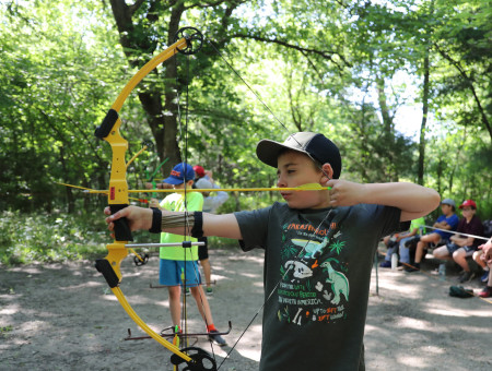 A camper learns how to aim a bow and arrow while attending summer camp at Rock Springs Ranch.