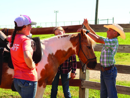 A Rock Springs Ranch staff member guides two campers as they care for a horse in the arena. Part of the equine program’s purpose is to teach hands-on skills, confidence, and compassion through horsemanship.
